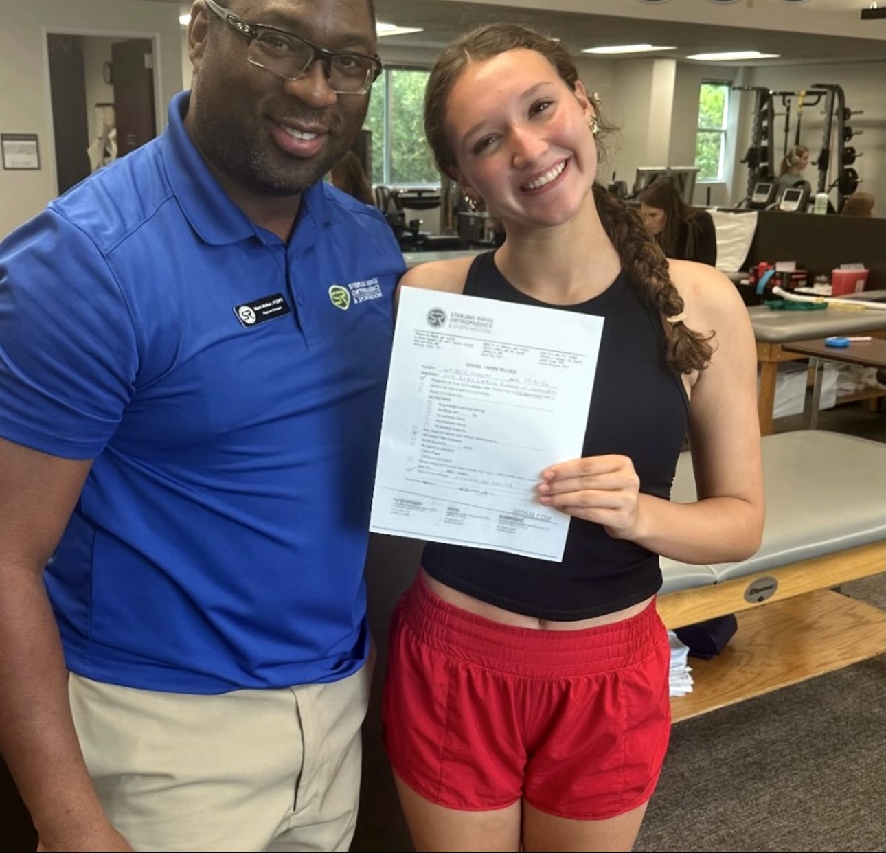 Natalie holding her return-to-play clearance with physical therapist Mark Walker at Sterling Ridge